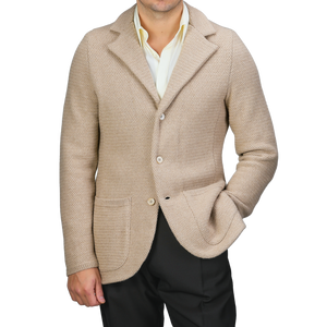 A person wearing a Stenströms Beige Merino Wool Knitted Blazer featuring a tailored waist, paired with a light yellow shirt and dark trousers, poses with one hand in their pocket against a plain backdrop.