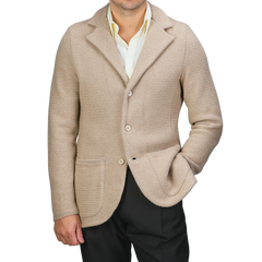 A person wearing a Stenströms Beige Merino Wool Knitted Blazer featuring a tailored waist, paired with a light yellow shirt and dark trousers, poses with one hand in their pocket against a plain backdrop.