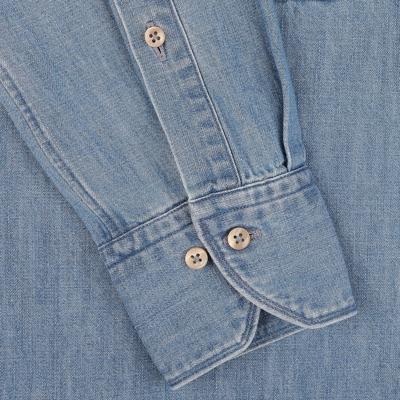 Close-up of a sleeve from the Stenströms Blue Washed Cotton Denim Slimline Shirt, crafted entirely from pure cotton denim. The slimline cut sleeve is detailed with two beige buttons that complement the matching denim fabric background.