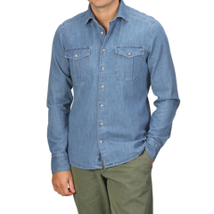 A person stands with one hand in a pocket, wearing the Stenströms Blue Washed Cotton Denim Slimline Shirt featuring two chest pockets and olive green pants.