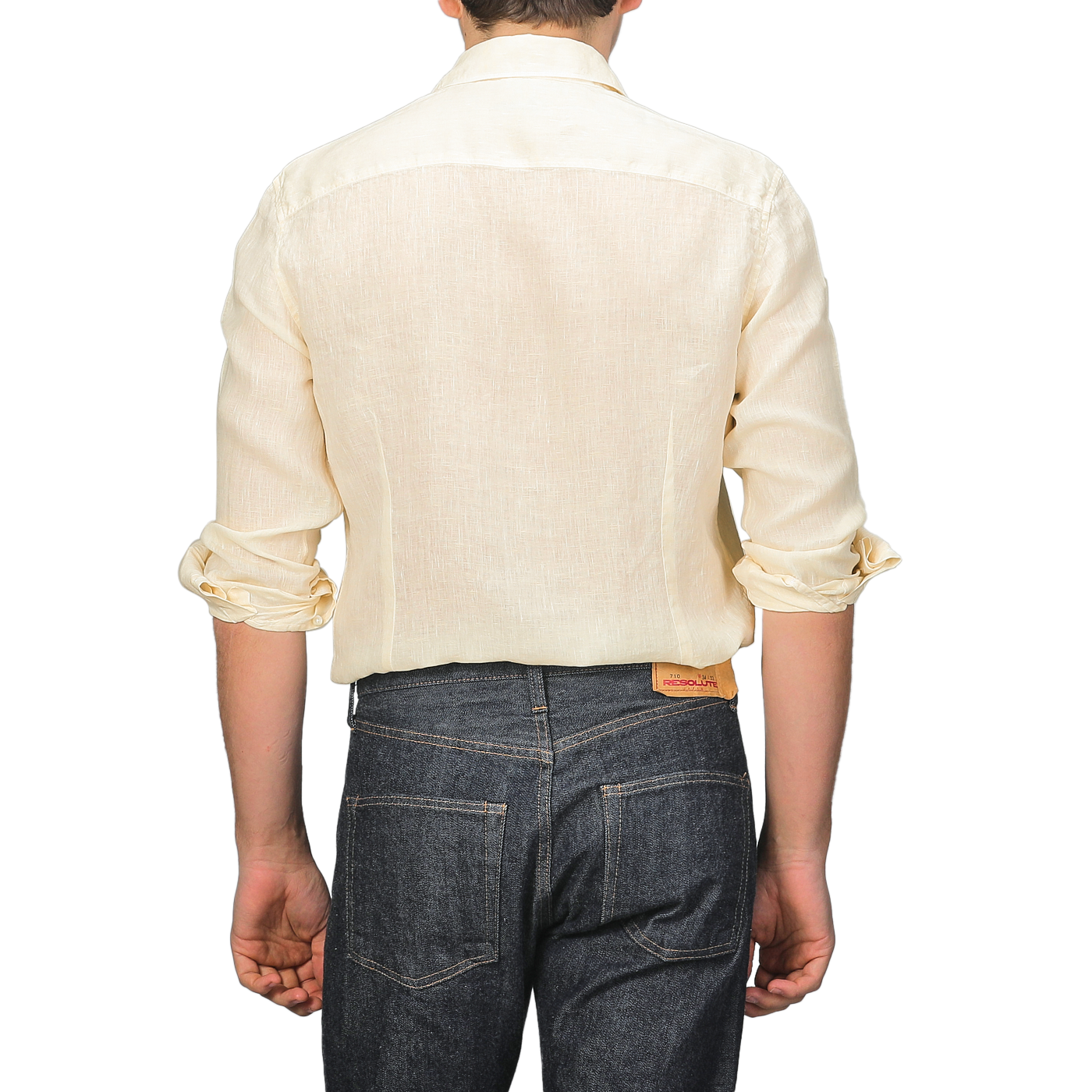 With their back to us, a person wears a Stenströms Butter Cream Linen Cutaway Slimline Shirt and dark jeans with rolled cuffs. This summer essential merges elegance and comfort, offering a stylish yet laid-back look against a plain backdrop.