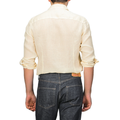 With their back to us, a person wears a Stenströms Butter Cream Linen Cutaway Slimline Shirt and dark jeans with rolled cuffs. This summer essential merges elegance and comfort, offering a stylish yet laid-back look against a plain backdrop.