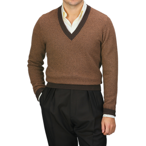 Dressed in a camel brown striped merino V-neck sweater by Stenströms over a crisp white shirt, the individual pairs this ensemble with sleek black pants, hands casually tucked into pockets.