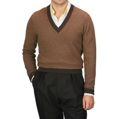 Dressed in a camel brown striped merino V-neck sweater by Stenströms over a crisp white shirt, the individual pairs this ensemble with sleek black pants, hands casually tucked into pockets.