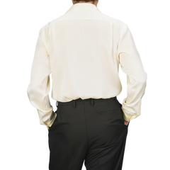 Individual dressed in a Cream Silk Fitted Body Shirt by Stenströms and black pants, facing away from the camera with hands tucked into pockets.