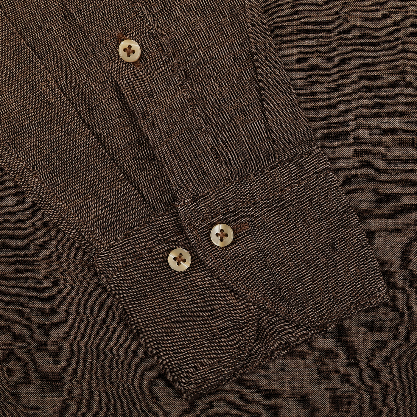 Close-up of a Stenströms Dark Brown Linen Cutaway Fitted Body Shirt with buttoned cuffs and tan buttons on a flat surface.