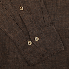 Close-up of a Stenströms Dark Brown Linen Cutaway Fitted Body Shirt with buttoned cuffs and tan buttons on a flat surface.