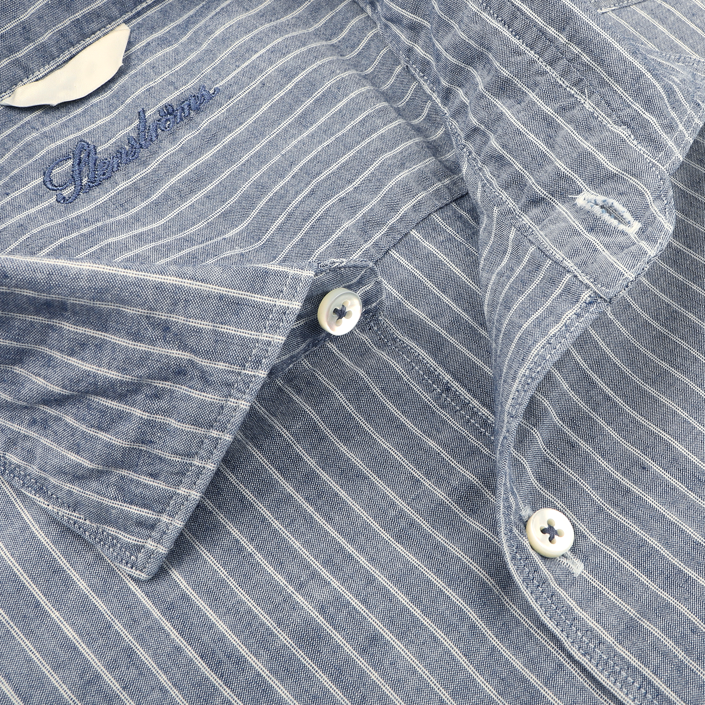 Close-up of Stenströms' Dark Indigo Striped Washed Cotton Fitted Body Shirt, showcasing a cut-away collar, white buttons, and an elegant embroidered logo on the chest in a blue and white striped pattern.