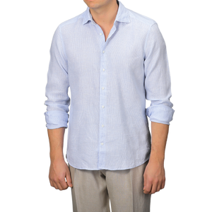 A man stands against a plain background effortlessly embracing summer style, wearing Stenströms' Light Blue Micro-Checked Linen Fitted Body Shirt with rolled-up sleeves and light-colored trousers.