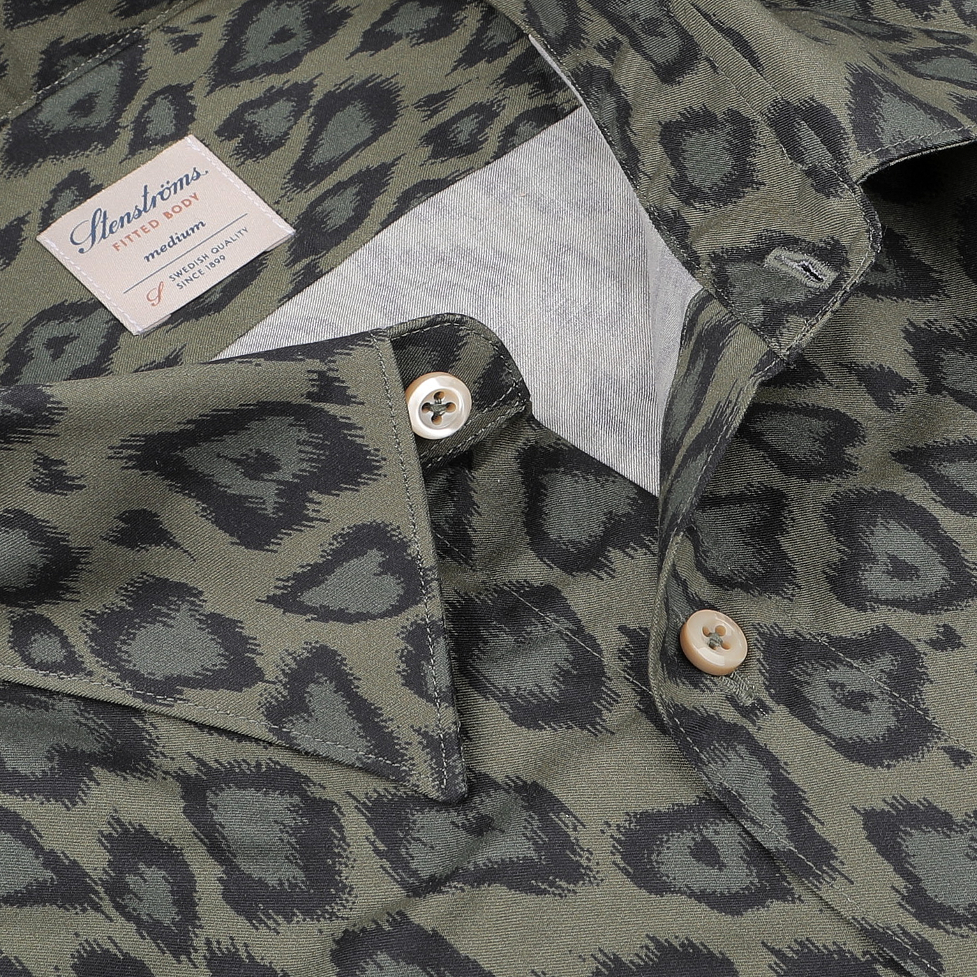 Close-up of the Green Animal Printed Fitted Body Shirt by Stenströms, showcasing its dark green fabric adorned with black leopard spots and a label that reads "Stenströms Fitted Body." Part of the brand's 125th birthday collection, this stylish shirt is crafted from a luxurious cotton-lyocell blend.