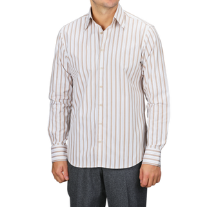 A man wearing a Stenströms Light Beige Striped Cotton Fitted Body Shirt pairs it with gray pants, confidently standing against a plain backdrop. His timeless style is highlighted by the pure cotton twill fabric.