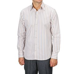 A man wearing a Stenströms Light Beige Striped Cotton Fitted Body Shirt pairs it with gray pants, confidently standing against a plain backdrop. His timeless style is highlighted by the pure cotton twill fabric.