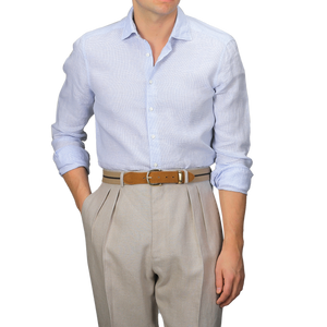 A man wears a Stenströms Light Blue Micro-Checked Linen Slimline Shirt paired with beige pleated trousers and a brown belt against a plain background. This summer essential offers a modern fit.