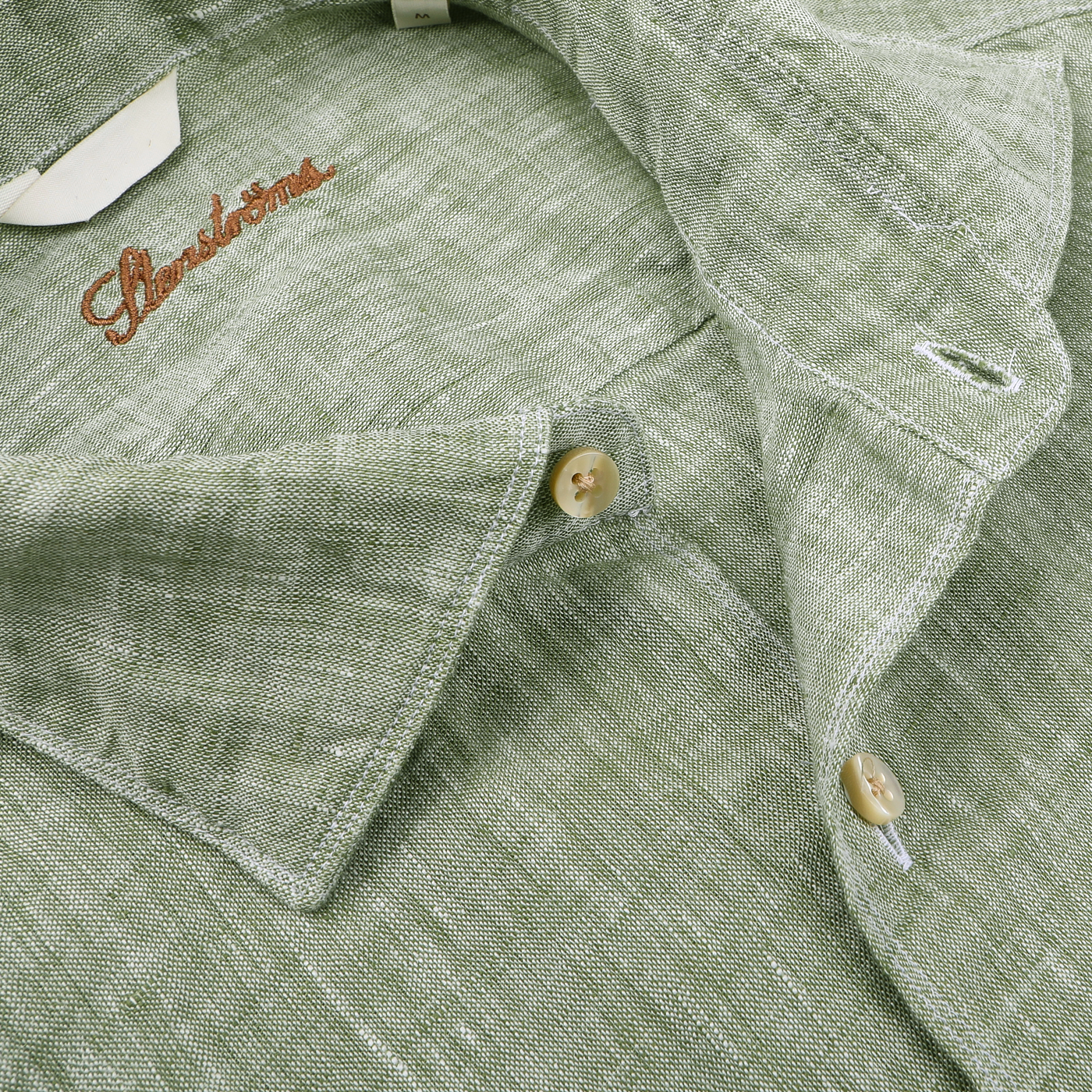 Close-up of the Stenströms Light Green Linen Cutaway Fitted Body Shirt featuring cream buttons and an embroidered brand name on the collar, making it a summer essential.