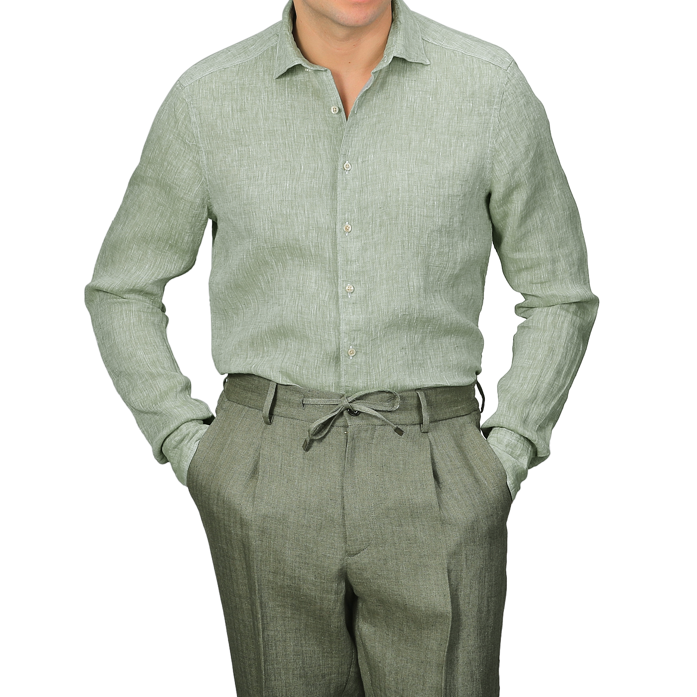 Clad in Stenströms' Light Green Linen Cutaway Slimline Shirt with mother of pearl buttons and coordinated slimline green trousers, a person stands with hands in pockets against a simple background, viewed from the shoulders down.