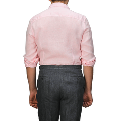 Viewed from the back, a person wears Stenströms' Light Pink Linen Cutaway Slimline Shirt with rolled-up sleeves and dark gray pants, showcasing a summer essential.