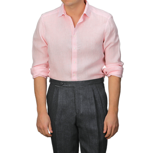 A person wears a Stenströms Light Pink Linen Cutaway Slimline Shirt with rolled-up sleeves, paired with dark gray pleated trousers. This summer essential's Slimline cut ensures a sleek and stylish look.