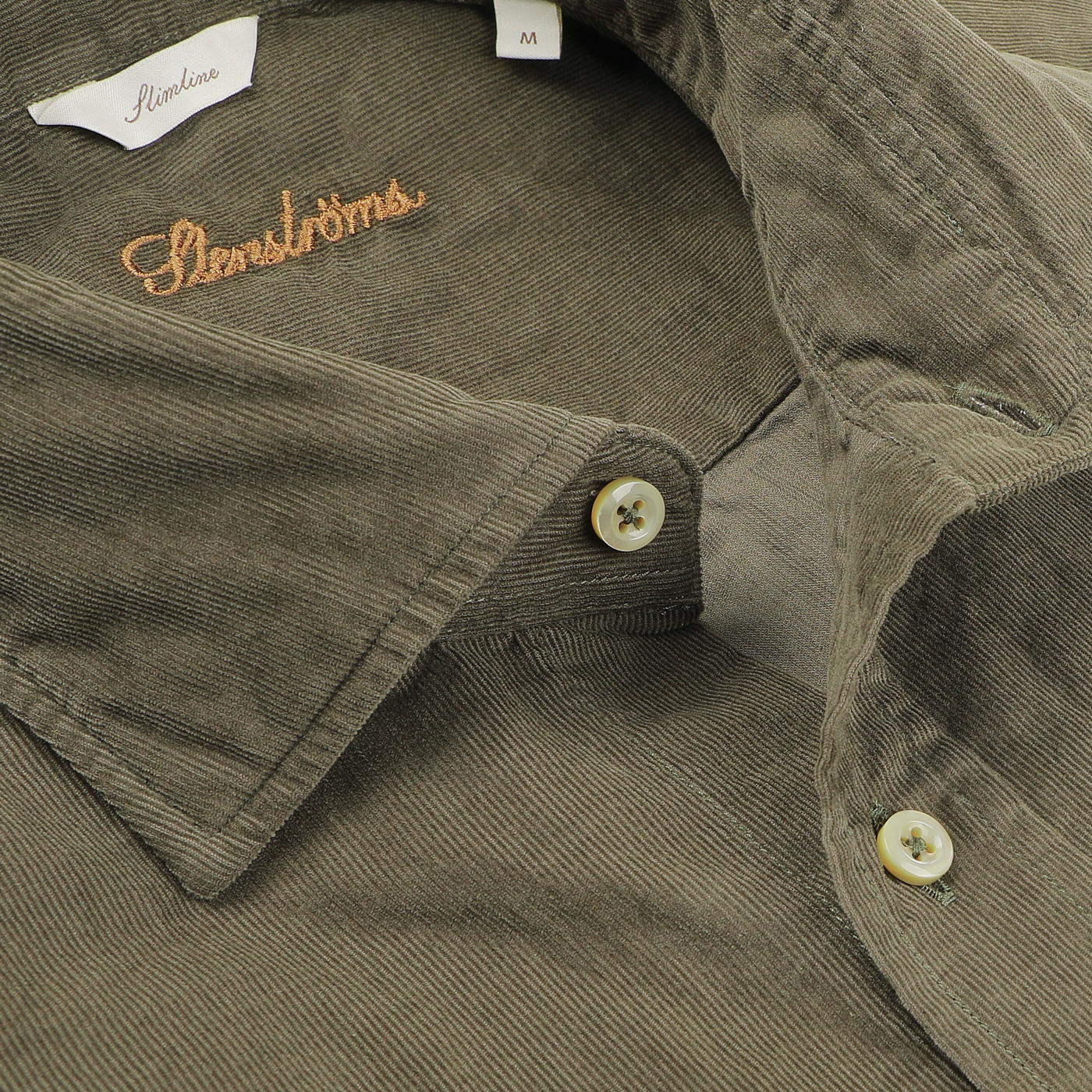 A close-up of a folded Moss Green Cotton Corduroy Slimline Shirt highlights its collar and buttons, with the Stenströms label visible near the collar.