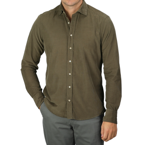 A man in a slimline cut, moss green shirt and gray pants stands with one hand in his pocket against a neutral background. The Stenströms Moss Green Cotton Corduroy Slimline Shirt adds a touch of elegance to his relaxed pose.