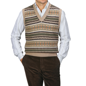 A person is standing against a gray background, wearing a Stenströms Taupe Beige Merino Wool Patterned Slipover over a striped shirt, paired with brown corduroy pants.