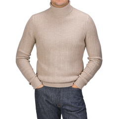 Person wearing a Taupe Beige Structured Merino Rollneck by Stenströms and dark jeans with hands in pockets, standing against a plain background.