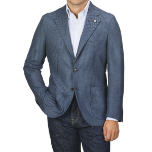 Man wearing a Blue Houndstooth Wool Flannel Blazer by Studio 73 over a white striped shirt and dark jeans, with hands in his pockets against a plain background.