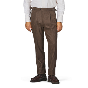 A person wearing a white long-sleeve shirt, Studio 73's Brown Melange Wool Flannel Pleated Trousers, and brown shoes stands against a plain background.