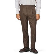 A person wearing a white long-sleeve shirt, Studio 73's Brown Melange Wool Flannel Pleated Trousers, and brown shoes stands against a plain background.