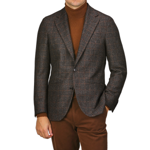 A person confidently wears the Dark Brown Checked Wool Cashmere Blazer by Studio 73, pairing it elegantly with a brown turtleneck and trousers, standing with one hand in their pocket.