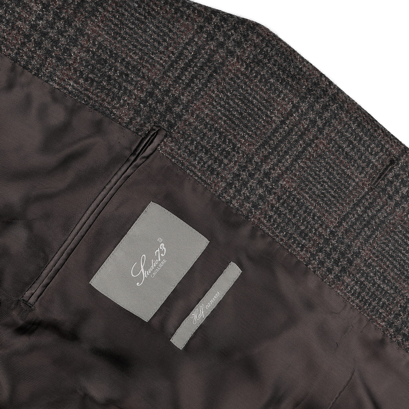 Close-up of a dark brown checked wool cashmere blazer's inner lining, featuring two labels. One label reads "Studio 73," and the other states "Half canvas." The luxurious lining is crafted from a wool-cashmere blend by Lanificio di Pray.