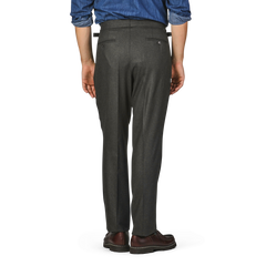 A person standing with their back facing the camera, wearing Studio 73 Dark Green Wool Flannel Pleated Trousers, a blue shirt, and brown shoes.