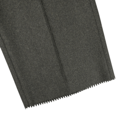 A close-up of the dark green fabric, featuring a zigzag cut hem that mirrors the refined texture characteristic of Studio 73's pure wool flannel Dark Green Wool Flannel Pleated Trousers, elegantly displayed on a white background.