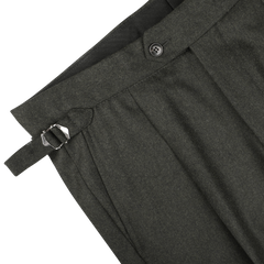 Close-up of the waistband of dark green wool flannel pleated trousers by Studio 73, featuring a single button, belt loops, and an adjustable side strap with a metal buckle.