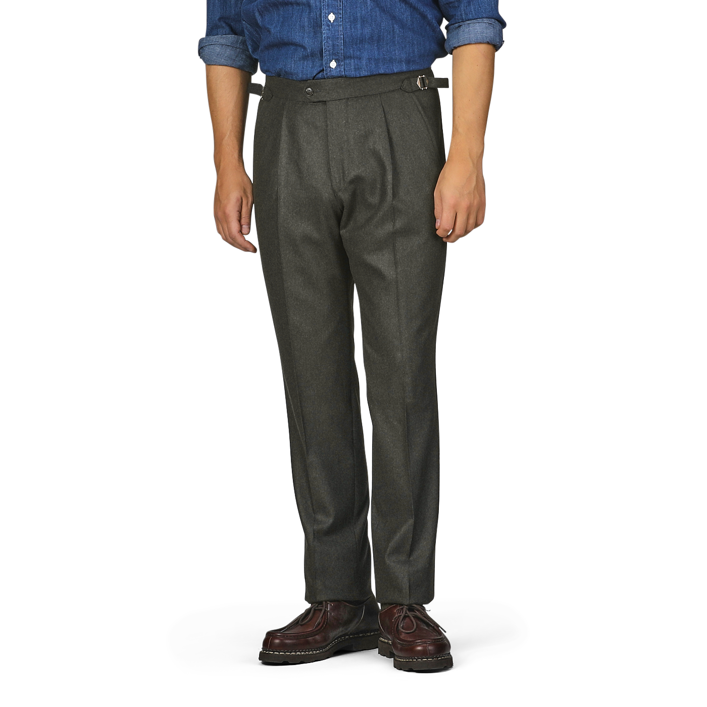 A person is standing wearing Studio 73's dark green wool flannel pleated trousers with a belt, a blue shirt with rolled-up sleeves, and brown shoes. The person's head and lower legs are outside the frame.