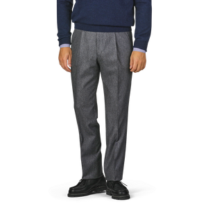 A person stands wearing a navy blue sweater, Studio 73 Dark Grey Wool Flannel Pleated Trousers, and black shoes. The image is cropped to show only the person from the waist down.