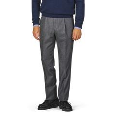 A person stands wearing a navy blue sweater, Studio 73 Dark Grey Wool Flannel Pleated Trousers, and black shoes. The image is cropped to show only the person from the waist down.