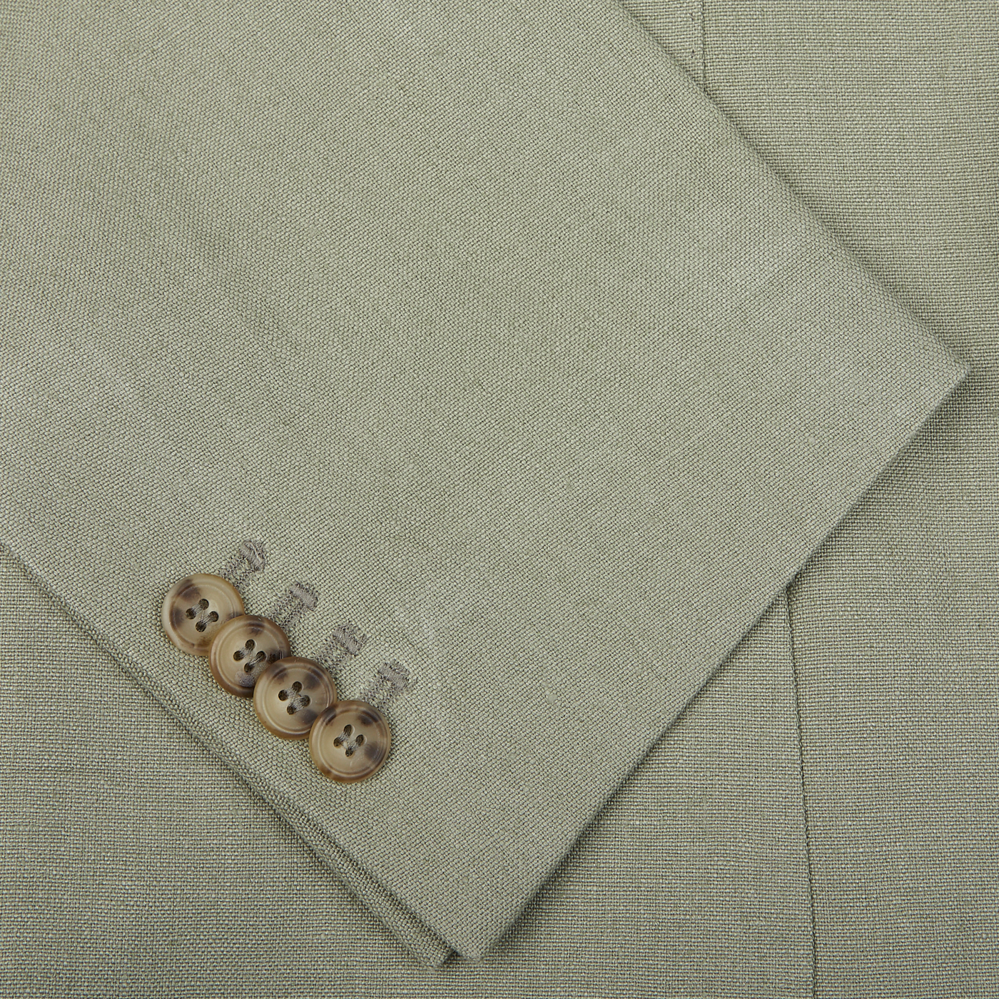 Close-up of a sage green Studio 73 suit sleeve with four brown buttons aligned near the cuff. The fabric texture is visibly woven, reflecting the quality of canapa hemp linen.
