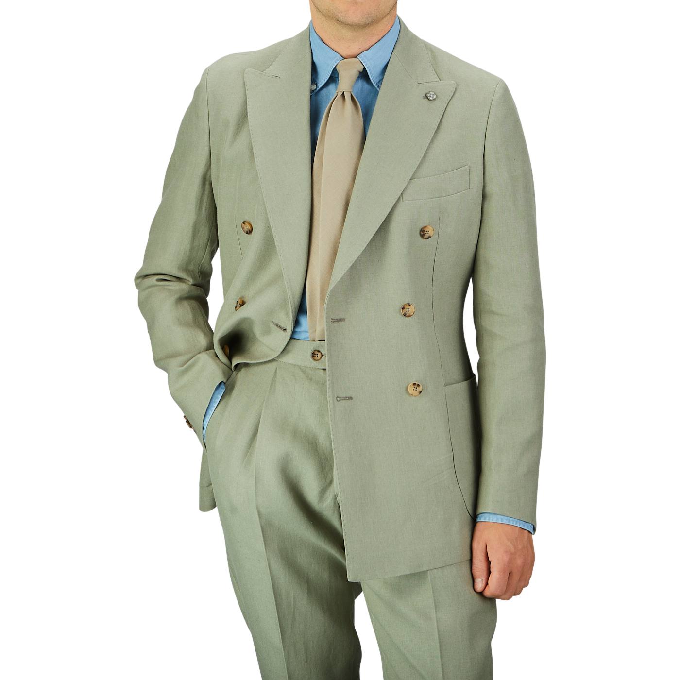 A person wearing a Sage Green Canapa Hemp DB Suit by Studio 73 with a light blue shirt and a beige tie stands with one hand in the pocket.