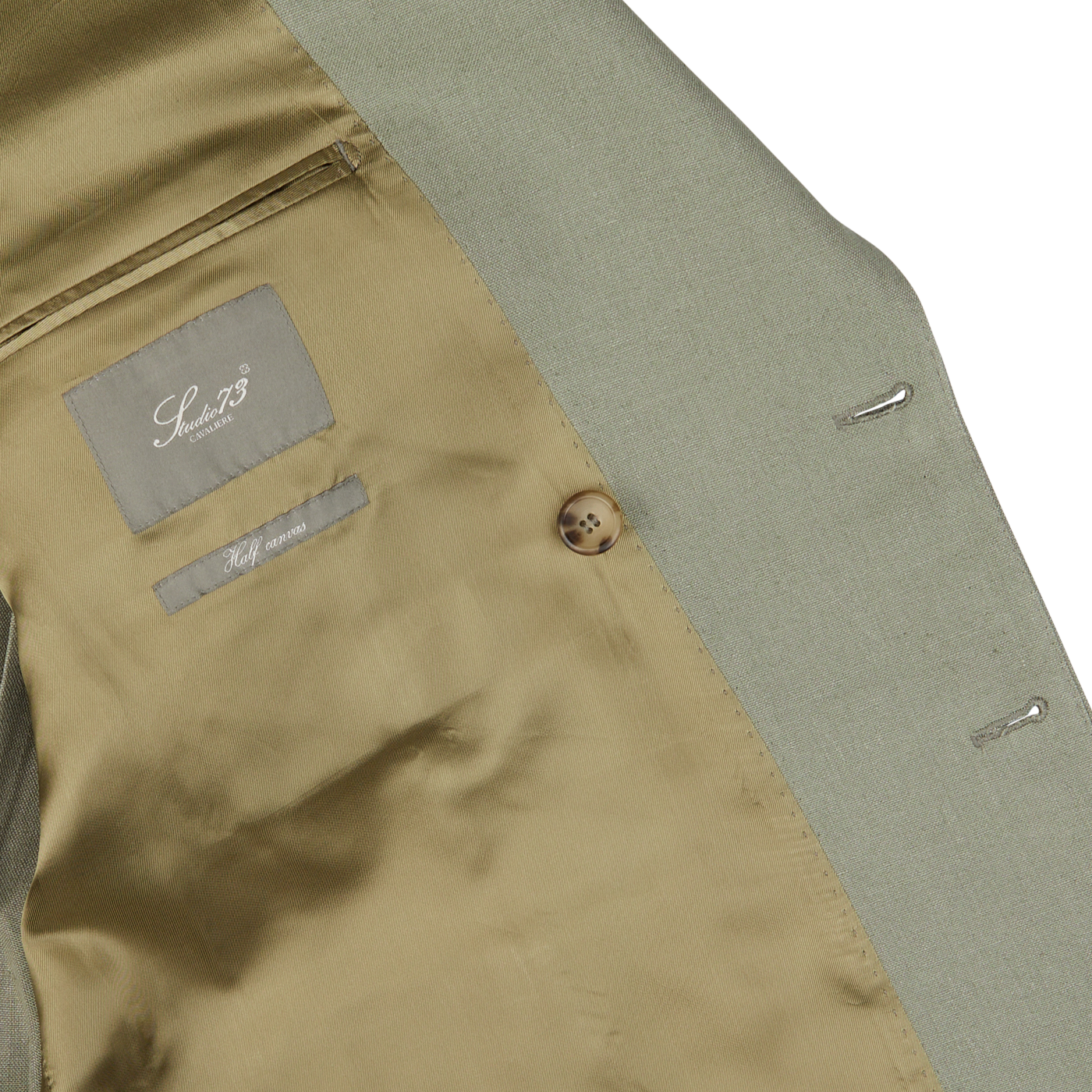 Close-up view of the inside of a Sage Green Canapa Hemp DB Suit featuring a brown button and a label with text in the inner pocket. This exquisite piece, crafted from luxurious Loro Piana canapa hemp linen, showcases impeccable attention to detail by Studio 73.