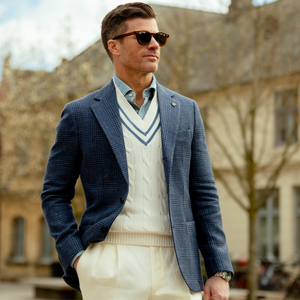 A stylish man in sunglasses, wearing a Studio 73 Dark Blue Checked Wool Linen Blazer, white sweater, and beige trousers outdoors.