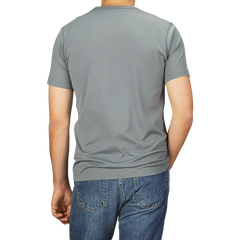 A person wearing a Smoke Green Classic Cotton T-Shirt by Sunspel and blue jeans is shown from the back.