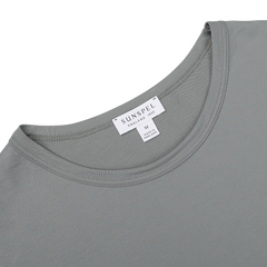 A close-up of a Sunspel Smoke Green Classic Cotton T-Shirt, showcasing the brand label on the neckline with size medium indicated. Crafted from premium cotton, this classic fit piece embodies timeless style and exceptional comfort.