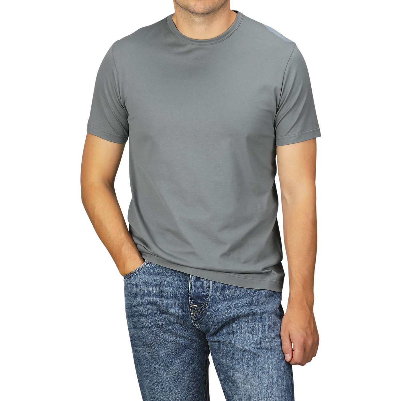 A man is standing against a plain background, wearing a Sunspel Smoke Green Classic Cotton T-Shirt and blue jeans. His left hand is in his jeans pocket. His head is not visible in the photo.