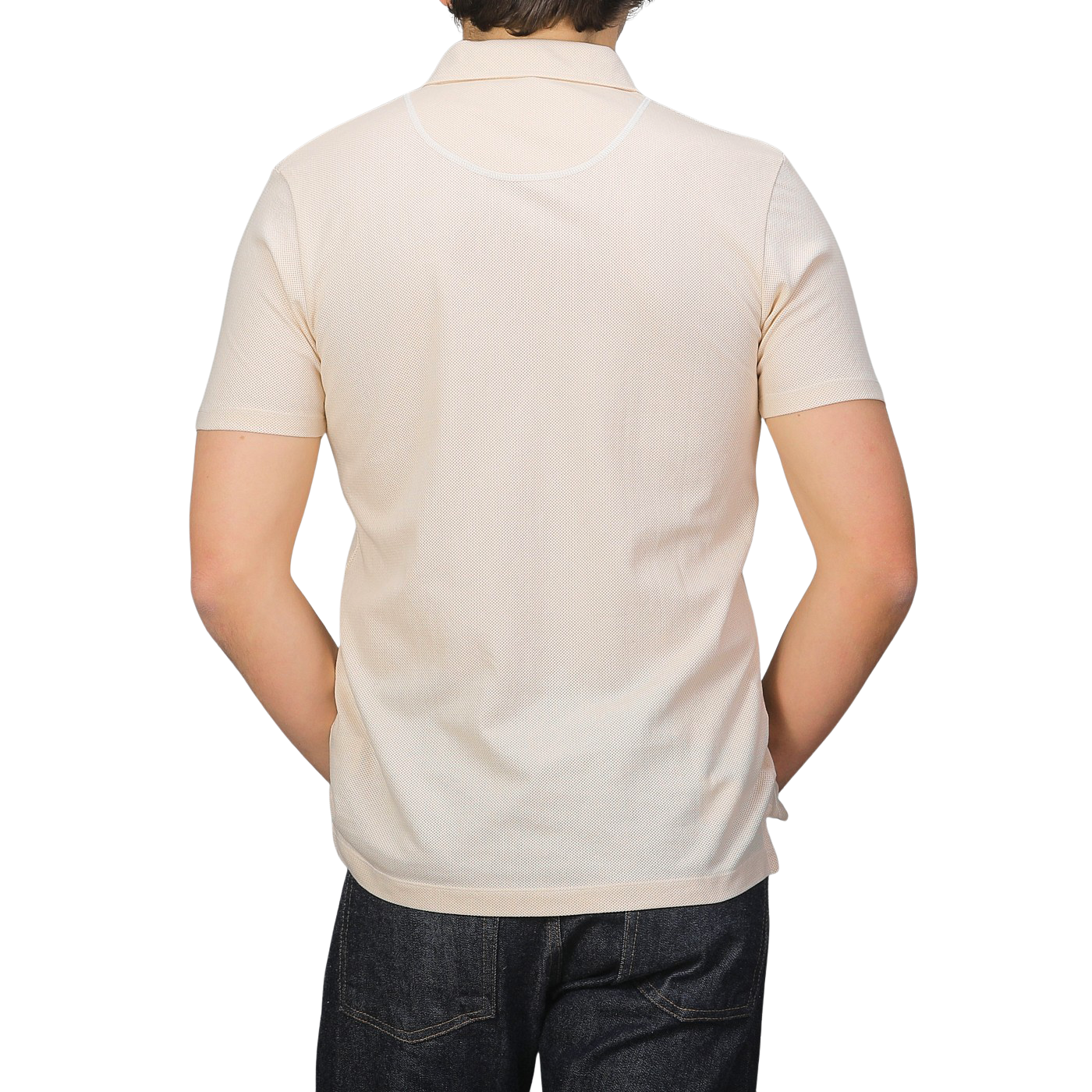 Rear view of a person in an ecru beige Sunspel Riviera polo shirt made from breathable cotton mesh, paired with dark jeans, against a plain background.