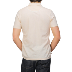 Rear view of a person in an ecru beige Sunspel Riviera polo shirt made from breathable cotton mesh, paired with dark jeans, against a plain background.