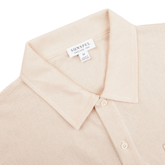 The Ecru Beige Cotton Riviera Polo Shirt by Sunspel is crafted in breathable cotton mesh with a buttoned collar, featuring a size M label. Made in Portugal, it offers both style and comfort.