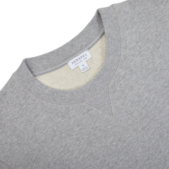 A close-up of the Grey Melange Cotton Loopback Sweatshirt by Sunspel, showcasing its plush texture and the visible label at the neckline that displays the brand name and size "M".