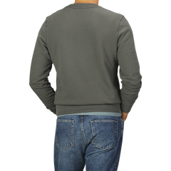 A person wearing a Khaki Green Cotton Loopback Sweatshirt by Sunspel and blue jeans is shown from the back against a plain background.