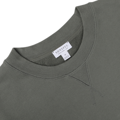 A close-up of a khaki green Sunspel Cotton Loopback Sweatshirt highlighting the collar, neckline stitching, and tag indicating size medium and cotton loopback fabric composition.