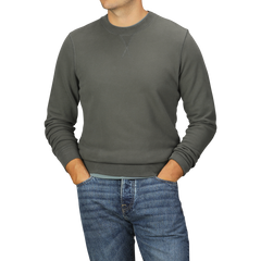 Person wearing a Khaki Green Cotton Loopback Sweatshirt by Sunspel and blue jeans, with hands in pockets, standing against a plain background.